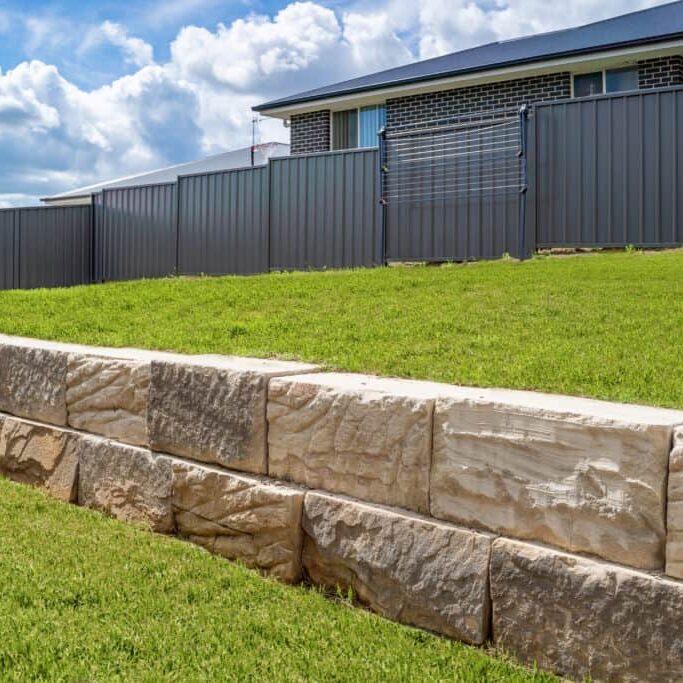 Stone retaining wall backyard green grass fence neighbour
